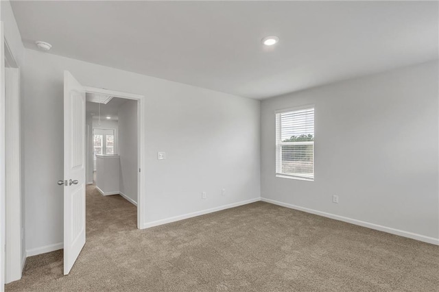 spare room featuring a healthy amount of sunlight, baseboards, attic access, and carpet flooring