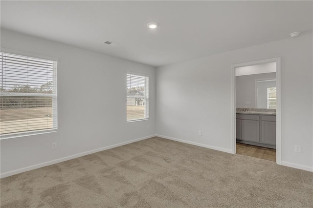 unfurnished bedroom featuring baseboards, carpet, ensuite bath, and visible vents