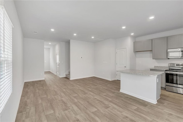 kitchen featuring appliances with stainless steel finishes, gray cabinets, light wood finished floors, and a center island