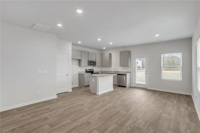 kitchen featuring baseboards, light countertops, gray cabinets, light wood finished floors, and appliances with stainless steel finishes