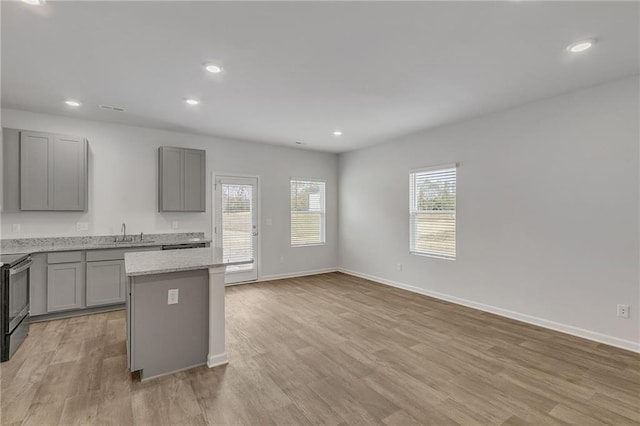 kitchen with gray cabinetry, light wood finished floors, a sink, and electric stove