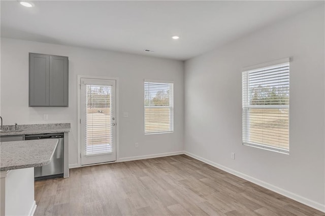 unfurnished dining area with baseboards, a sink, and light wood-type flooring
