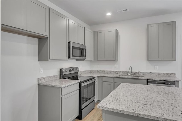 kitchen featuring gray cabinets, visible vents, appliances with stainless steel finishes, light wood-type flooring, and a sink