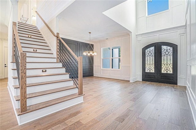 foyer with light wood-style flooring, a chandelier, french doors, a decorative wall, and stairs