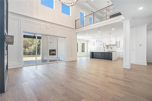 unfurnished living room with a towering ceiling, wood finished floors, a glass covered fireplace, and decorative columns