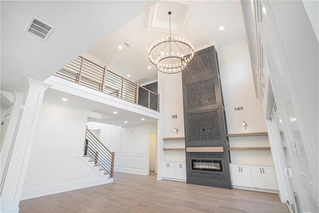 unfurnished living room with wood finished floors, stairs, a fireplace, visible vents, and a high ceiling