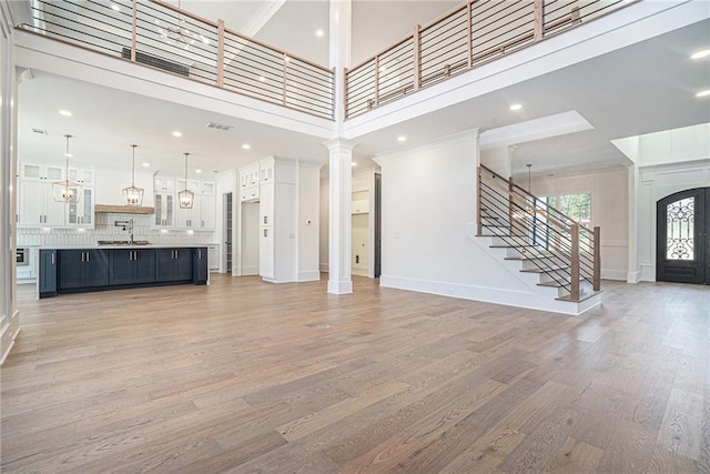 unfurnished living room with a high ceiling, a sink, stairway, light wood-type flooring, and visible vents
