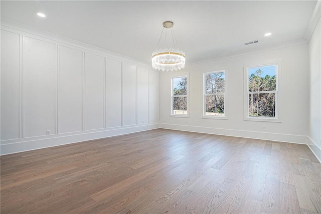 unfurnished dining area featuring a notable chandelier, visible vents, wood finished floors, and a decorative wall