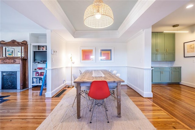 dining area featuring light wood finished floors, ornamental molding, wainscoting, a tray ceiling, and an inviting chandelier