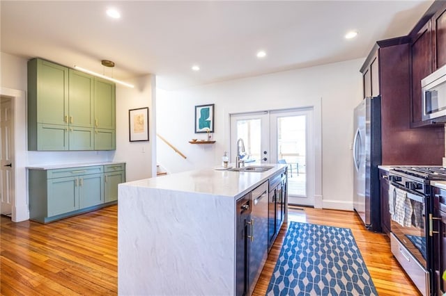 kitchen with a center island with sink, stainless steel appliances, light wood-style floors, a sink, and green cabinetry