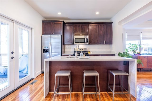 kitchen with stainless steel appliances, a breakfast bar, a sink, french doors, and backsplash