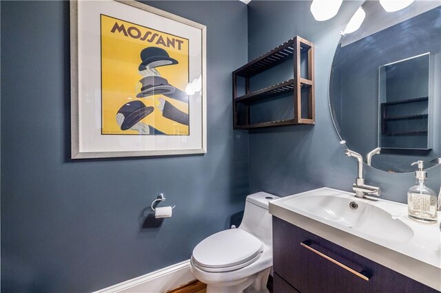 half bathroom featuring toilet, baseboards, and vanity