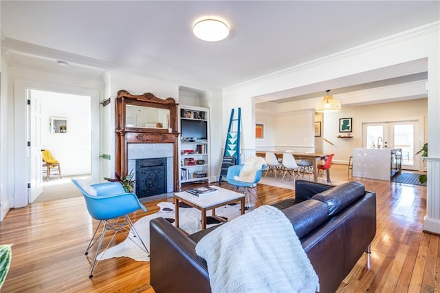 living area featuring a fireplace with flush hearth, ornamental molding, light wood-style flooring, and french doors