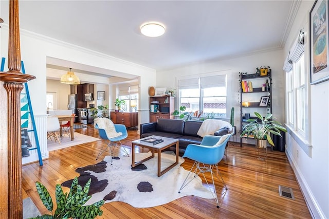 living room with ornamental molding, baseboards, visible vents, and light wood finished floors