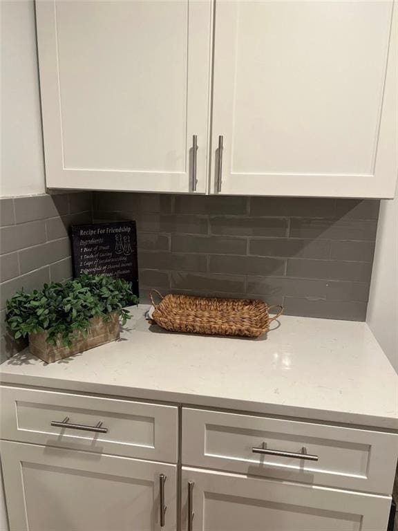 room details with backsplash, light stone countertops, and white cabinets