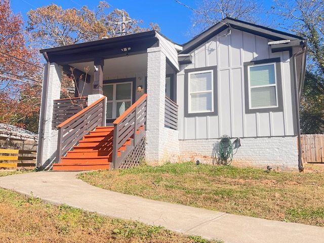 view of front of house with a porch, board and batten siding, fence, a front lawn, and stairs