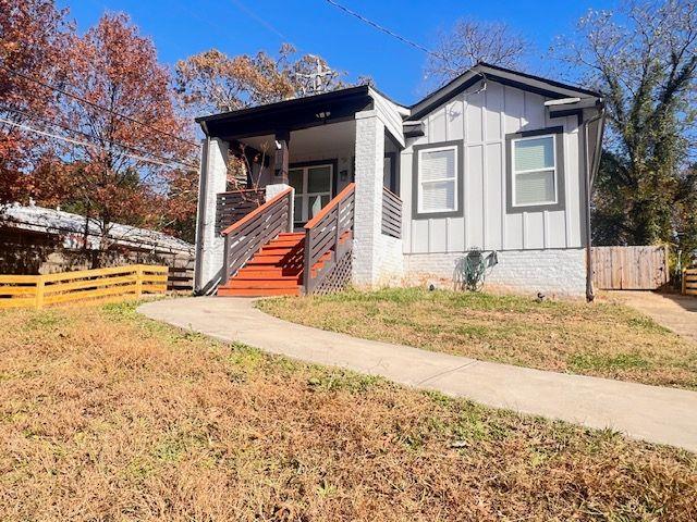 bungalow-style house featuring covered porch, fence, a front lawn, and board and batten siding