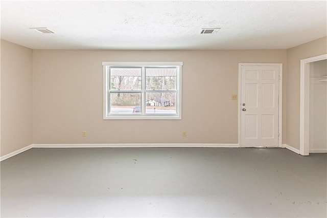 empty room with concrete flooring, a textured ceiling, visible vents, and baseboards