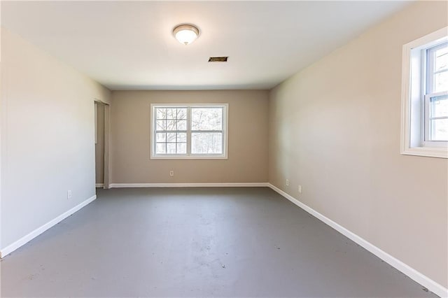 unfurnished room with finished concrete flooring, visible vents, and baseboards