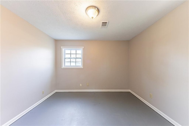 spare room featuring finished concrete floors, visible vents, a textured ceiling, and baseboards