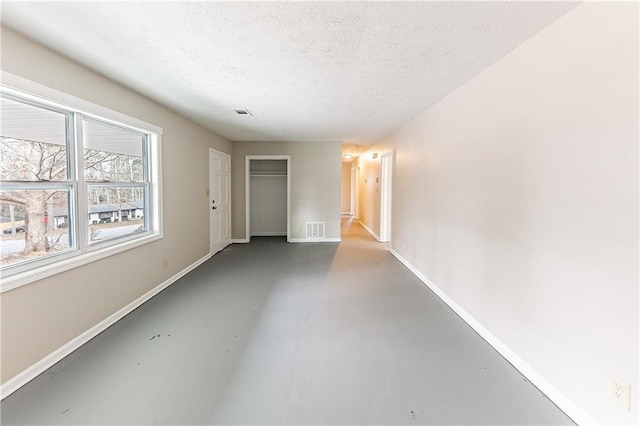 spare room featuring baseboards, concrete floors, visible vents, and a textured ceiling