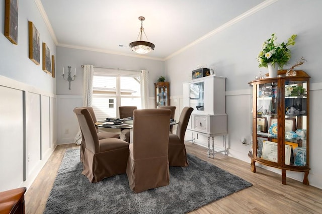 dining room with a wainscoted wall, light wood-type flooring, and crown molding