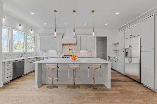 kitchen with a center island, light hardwood / wood-style flooring, decorative backsplash, appliances with stainless steel finishes, and custom range hood