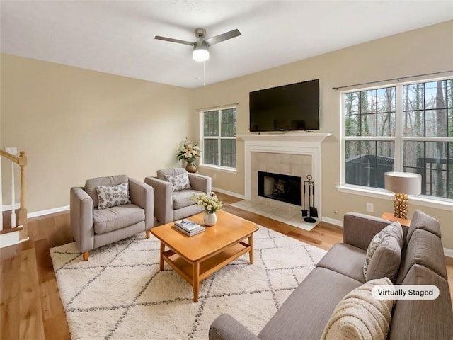 living room featuring ceiling fan, light hardwood / wood-style floors, a tile fireplace, and a healthy amount of sunlight