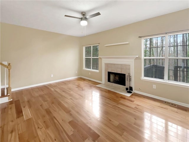 unfurnished living room featuring plenty of natural light, a tiled fireplace, and light hardwood / wood-style flooring