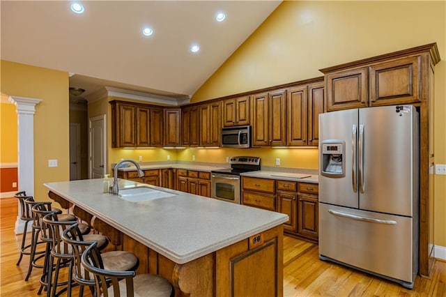 kitchen featuring appliances with stainless steel finishes, light wood-type flooring, a kitchen breakfast bar, a kitchen island with sink, and sink