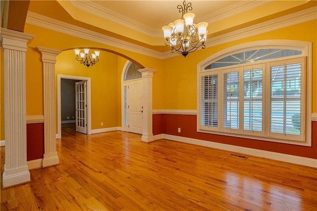 spare room with a notable chandelier, a raised ceiling, ornate columns, and ornamental molding