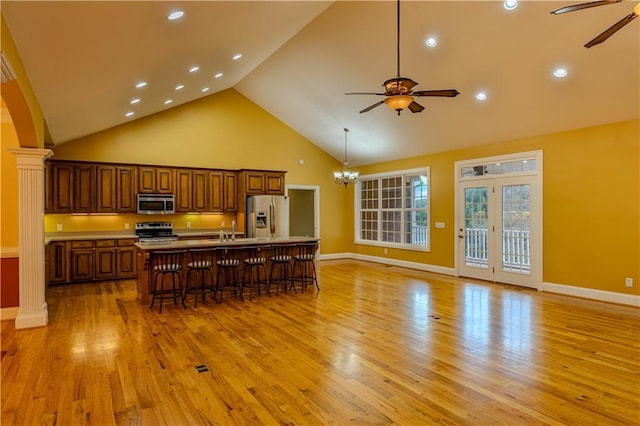 kitchen featuring a breakfast bar, a center island with sink, sink, appliances with stainless steel finishes, and decorative columns