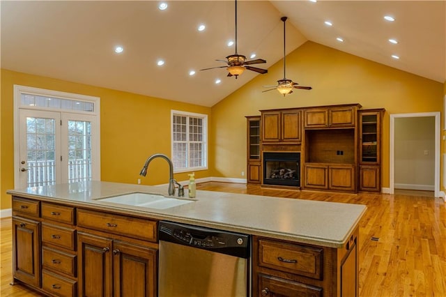 kitchen with stainless steel dishwasher, ceiling fan, a kitchen island with sink, sink, and light hardwood / wood-style floors