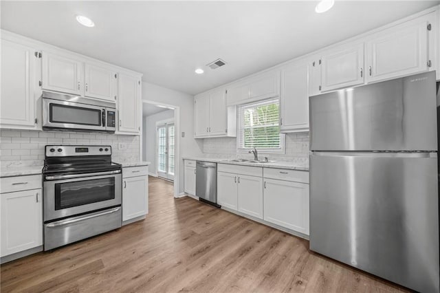 kitchen featuring sink, light hardwood / wood-style flooring, appliances with stainless steel finishes, light stone counters, and white cabinets