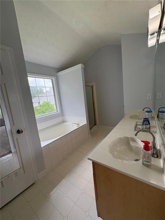 1951 Bergerac Ct SW, Marietta, GA 30008 - full bathroom featuring double vanity, a bath, vaulted ceiling, and a textured ceiling
