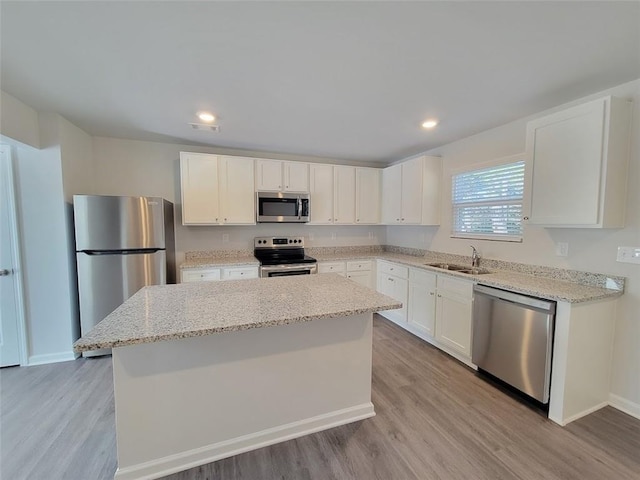 kitchen with sink, appliances with stainless steel finishes, light stone countertops, white cabinets, and a kitchen island