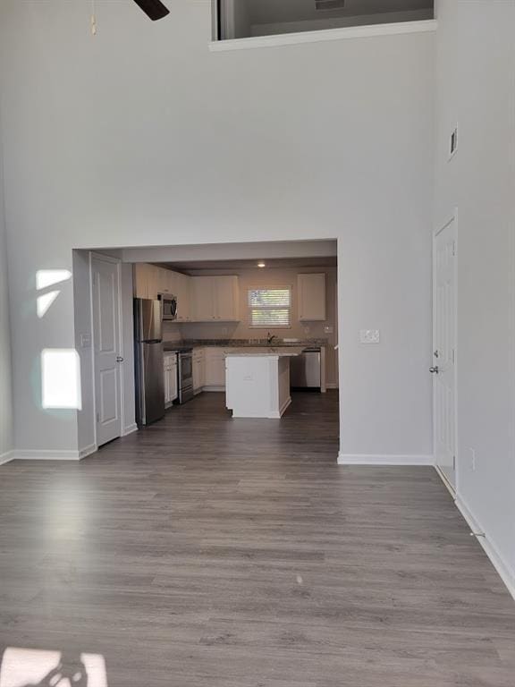 unfurnished living room featuring light wood-type flooring, ceiling fan, and a high ceiling