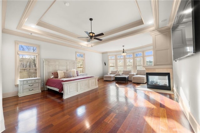 bedroom featuring ornamental molding, a tray ceiling, dark wood-style flooring, and a multi sided fireplace