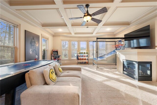 playroom featuring coffered ceiling, a glass covered fireplace, beamed ceiling, crown molding, and carpet flooring