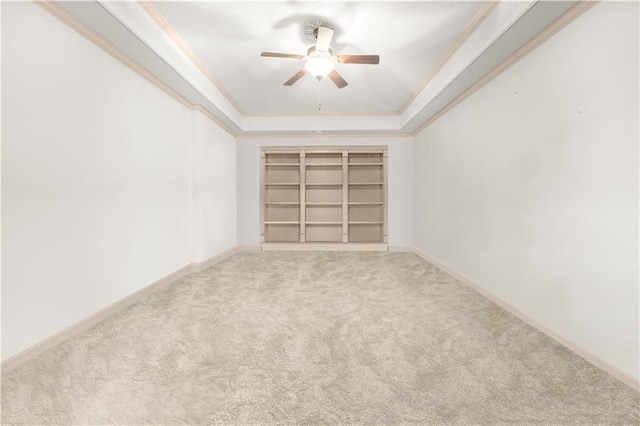 carpeted empty room featuring a ceiling fan, a tray ceiling, baseboards, and crown molding