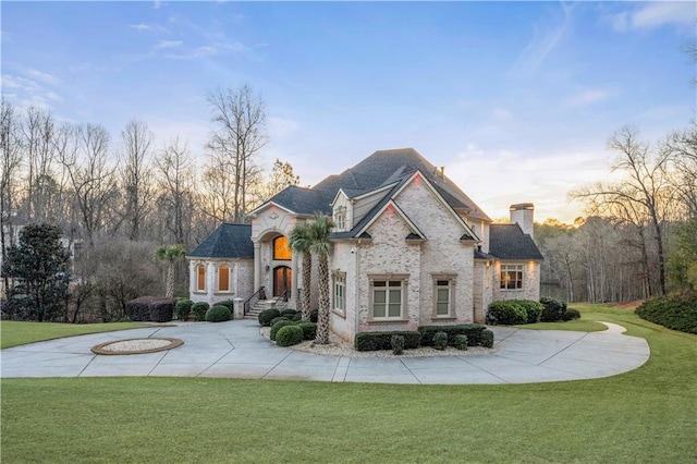 french country style house featuring a chimney, curved driveway, and a front lawn