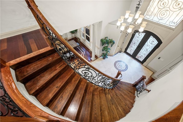 entryway featuring wood finished floors, a towering ceiling, baseboards, stairway, and an inviting chandelier