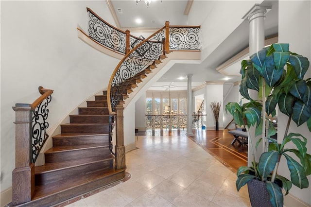 stairs with crown molding, baseboards, decorative columns, and a high ceiling