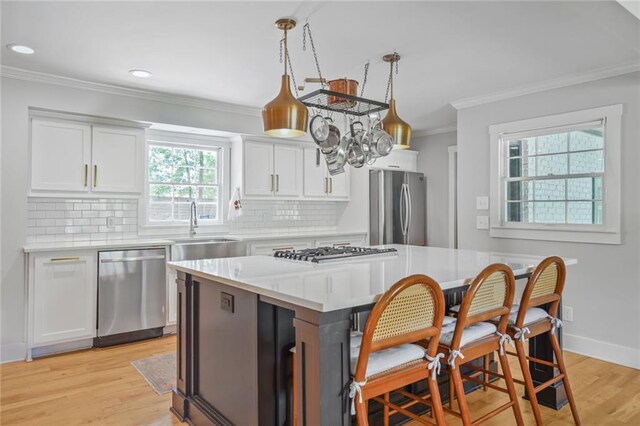kitchen featuring stainless steel appliances, a sink, crown molding, backsplash, and light countertops