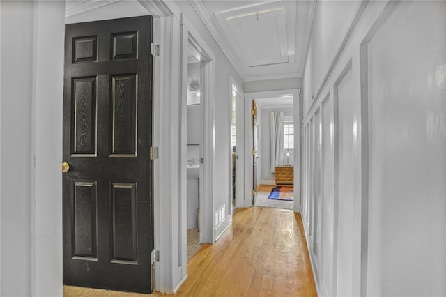 corridor with attic access, light wood finished floors, and ornamental molding