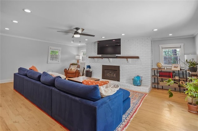 living room with ornamental molding, light wood-style floors, a brick fireplace, a ceiling fan, and recessed lighting