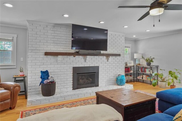 living area featuring ornamental molding, wood finished floors, a brick fireplace, recessed lighting, and a ceiling fan