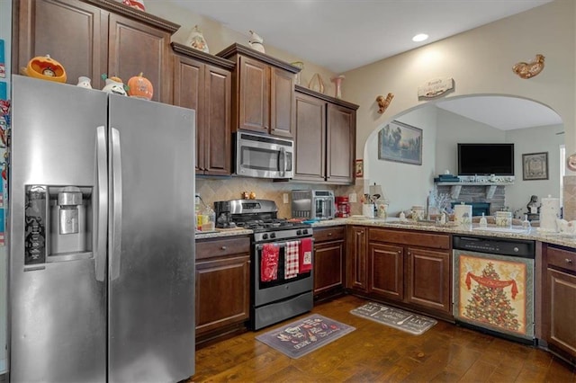 kitchen with dark wood-type flooring, stainless steel appliances, backsplash, sink, and light stone counters