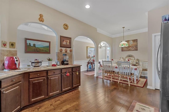 kitchen featuring dark brown cabinets, pendant lighting, dark wood-type flooring, light stone counters, and stainless steel refrigerator