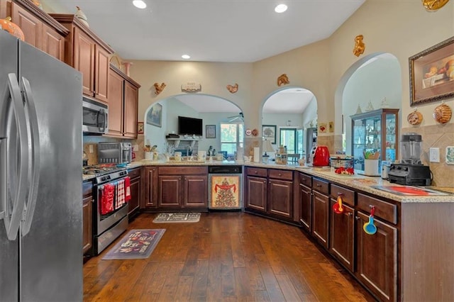 kitchen with kitchen peninsula, tasteful backsplash, stainless steel appliances, and dark wood-type flooring